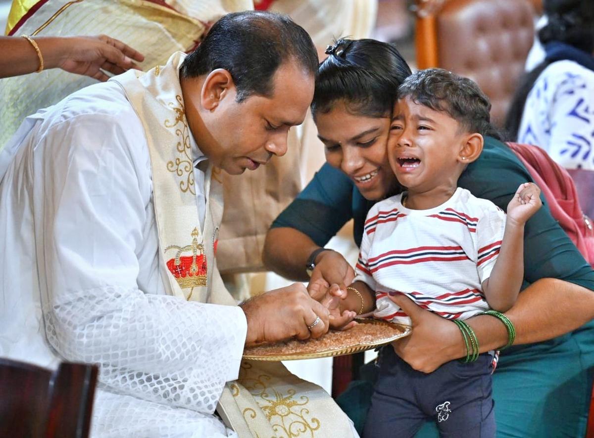 एक चर्च पुजारी एक बच्चे को मलयालम में अपने पहले पत्रों के माध्यम से मादरीबहम समारोह के दौरान माद्रे ड्यूस चर्च, वेतुटोकाउड, तिरुवनंतपुरम में थिरुवनंतपुरम में थिरुवनंतपुरम का मार्गदर्शन करता है।